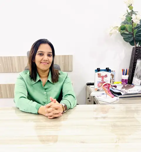 A doctor sitting at a consultation desk, smiling, with a uterus anatomical model and a printed diagram on the desk beside her.